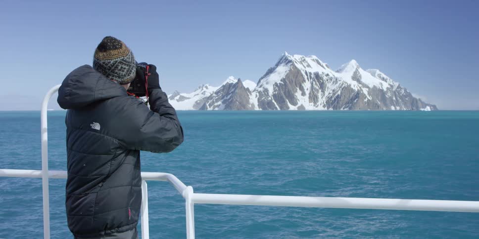 A man stands by the railing of a boat taking photographs