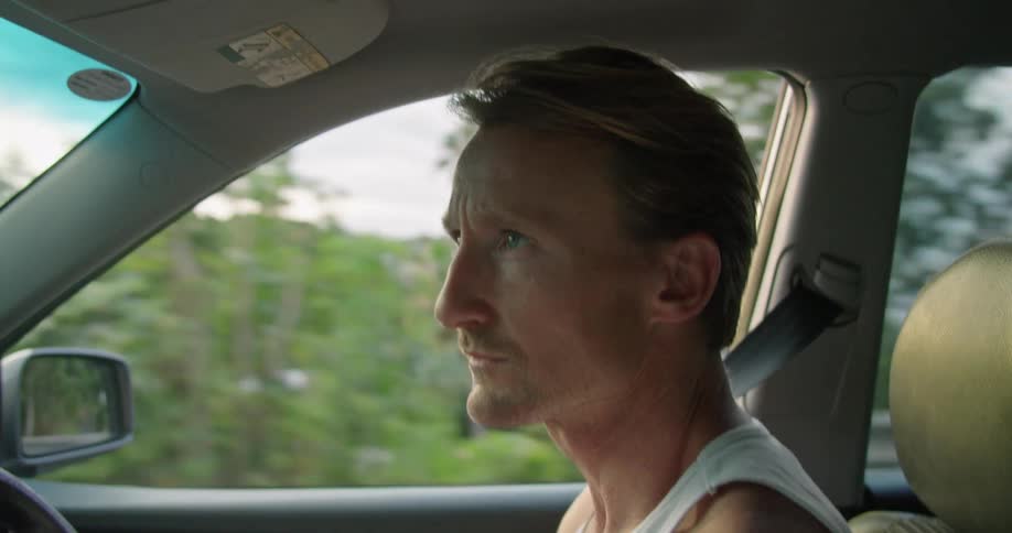 A man looks around while driving through a tropical town