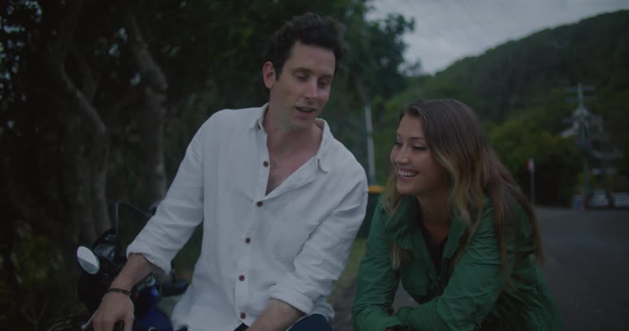 Man and woman lean against motorcycle parked near road talking and smiling