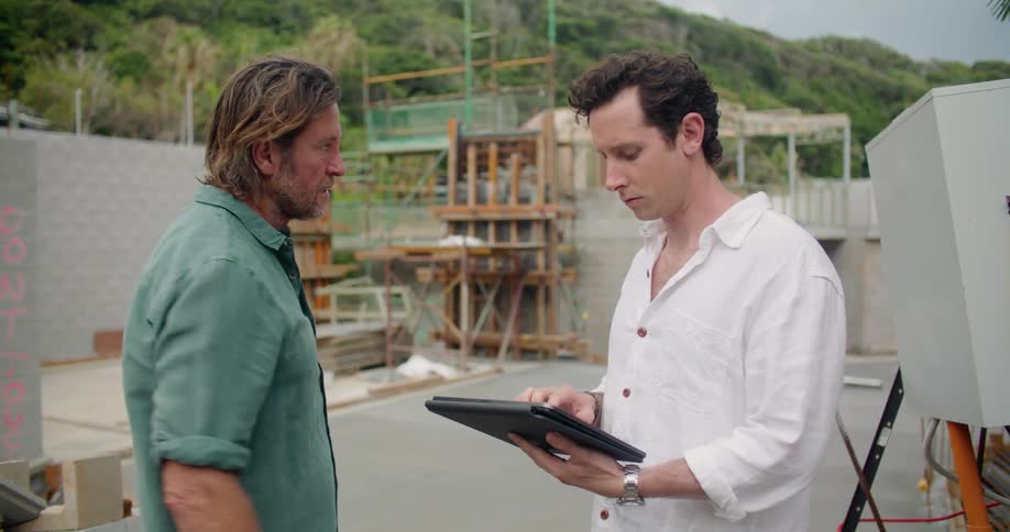 Two men look at a tablet and talk on a work site