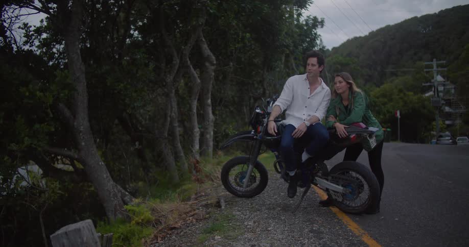 Couple reclined on a parked motorcycle on a road in the countryside talking