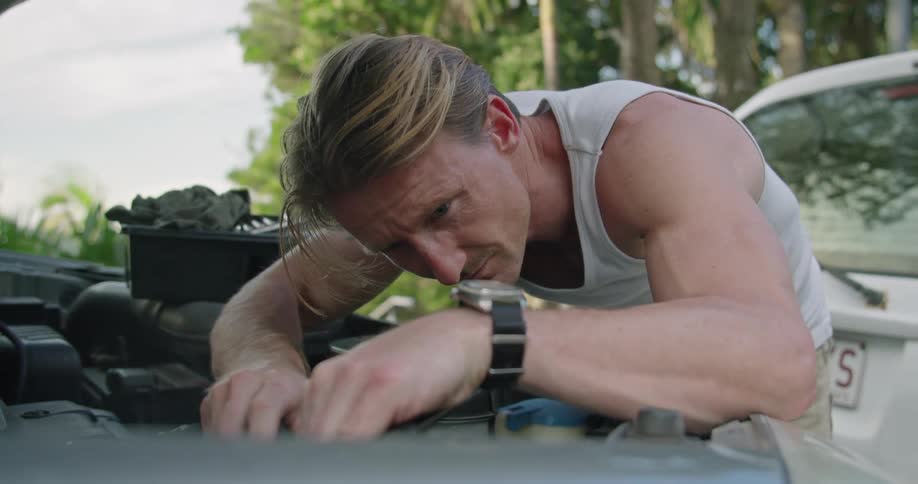 A man uses a screwdriver while working under the hood of his car