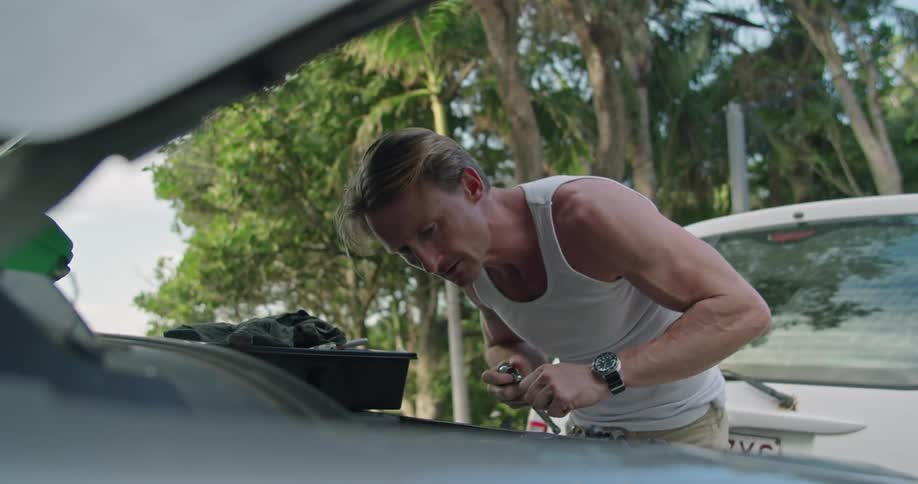 A man uses a socket wrench to repair his car engine outside