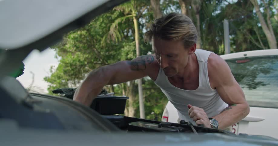 A man uses a wrench while working on his cars engine