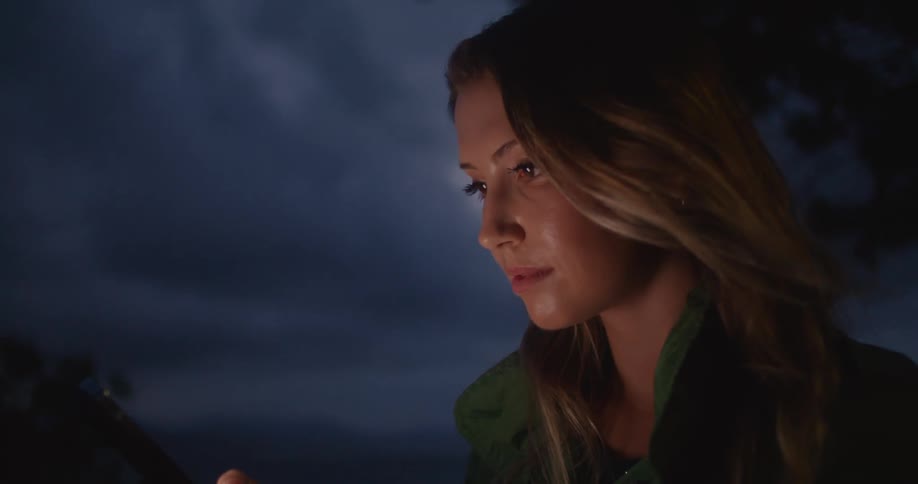 Woman with brown hair swipes down on smartphone outdoors at night