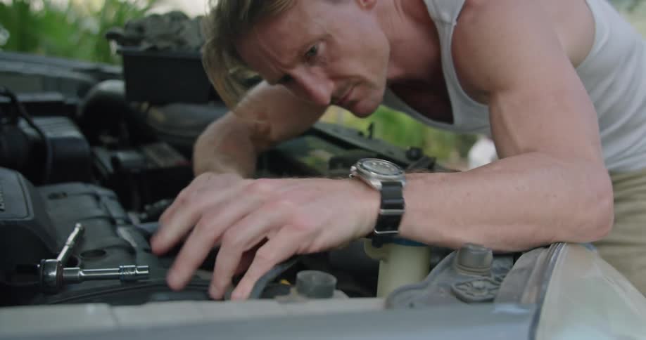 A man tightens a screw while working on his car engine