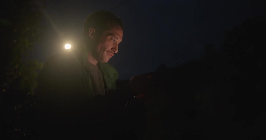 A man is using a cellphone in the dark with a light shining brightly behind him