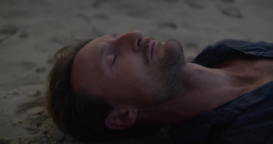 Man lying on his back on sandy beach opens his eyes