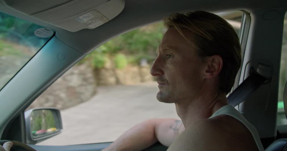 A man drives through a neighborhood with an arm resting out the window