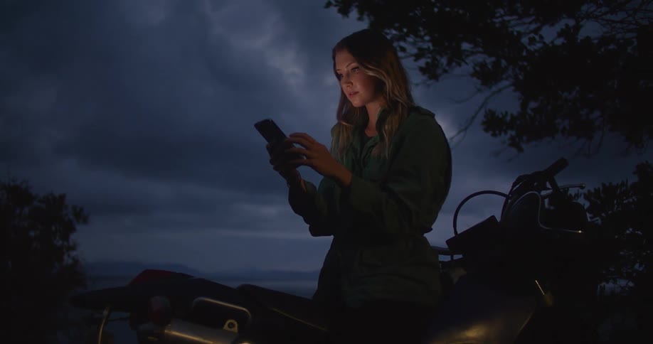 A woman is standing outside near a tree on a dark night