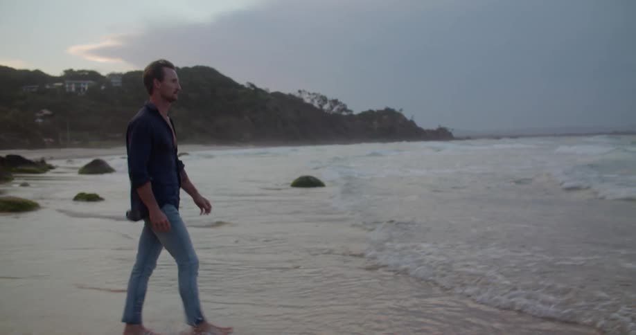 A lone man walking and splashing barefoot on a sandy beach