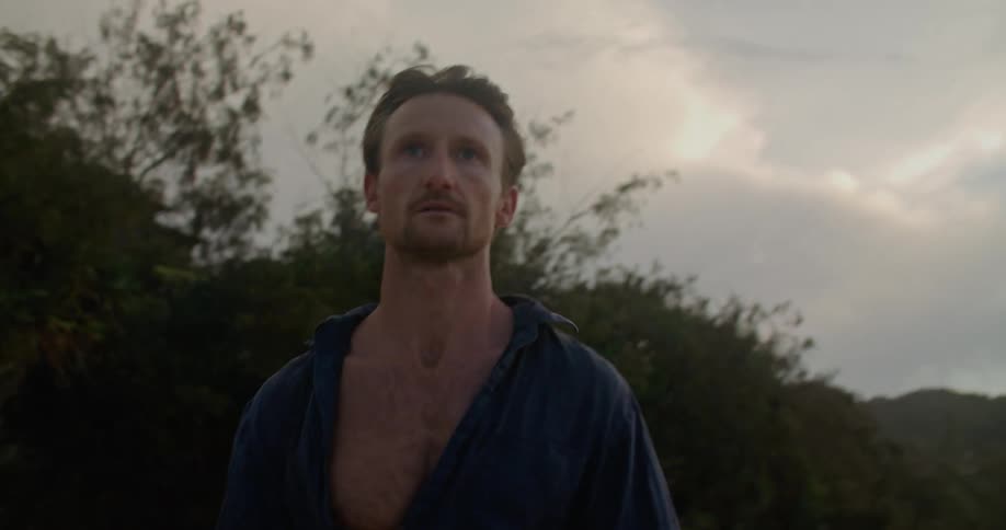 A man is staring off and walking on an ocean beach on a windy evening