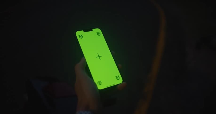 A person is holding a cell phone with a plus sign on a green screen