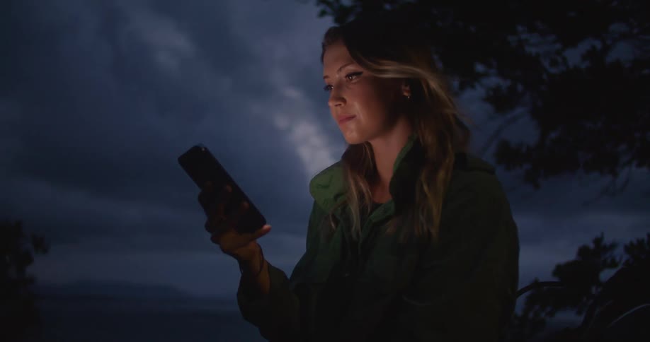 A woman is standing outdoors with a cell phone next to a motorcycle