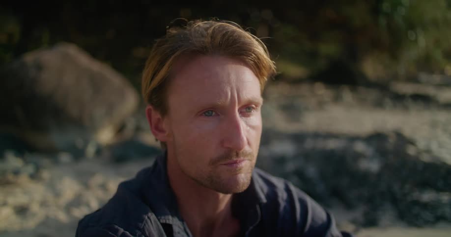 Man sits on beach wiping his face as he cries