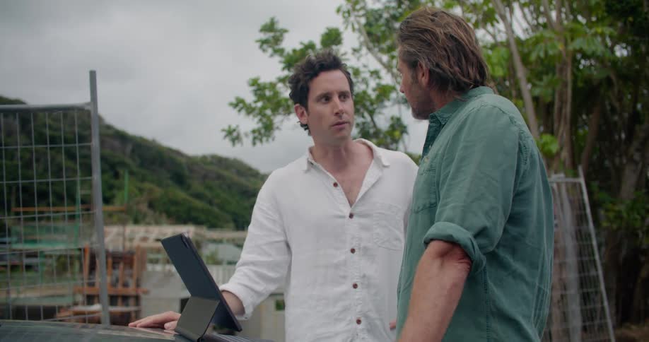 Two men standing outside near a construction site having a meeting with a laptop on a car hood