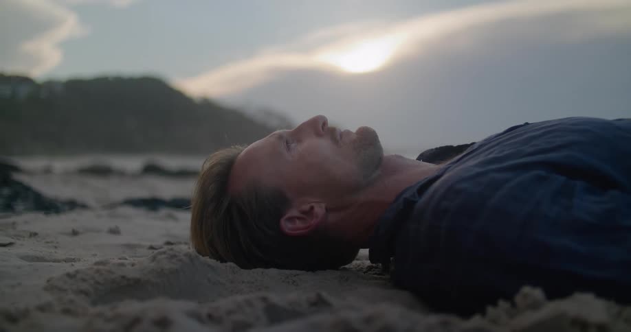 A man lies down on wet sand on the beach