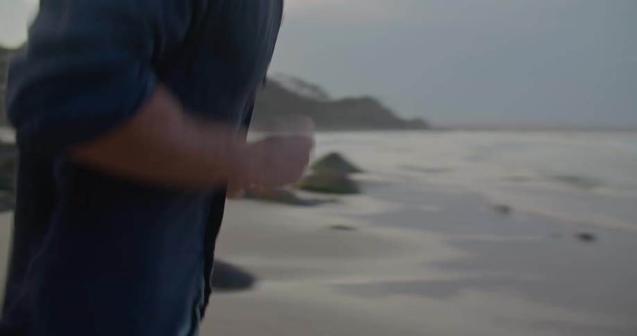 Man removes his wristwatch then runs across beach toward surf