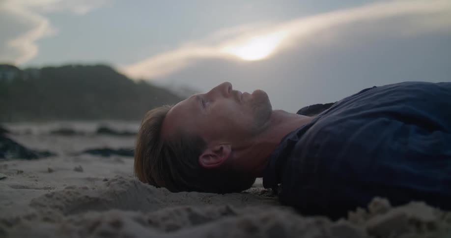 A man lying on the sand staring up at the sky