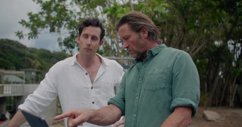 Two men are talking outdoors and looking at a laptop