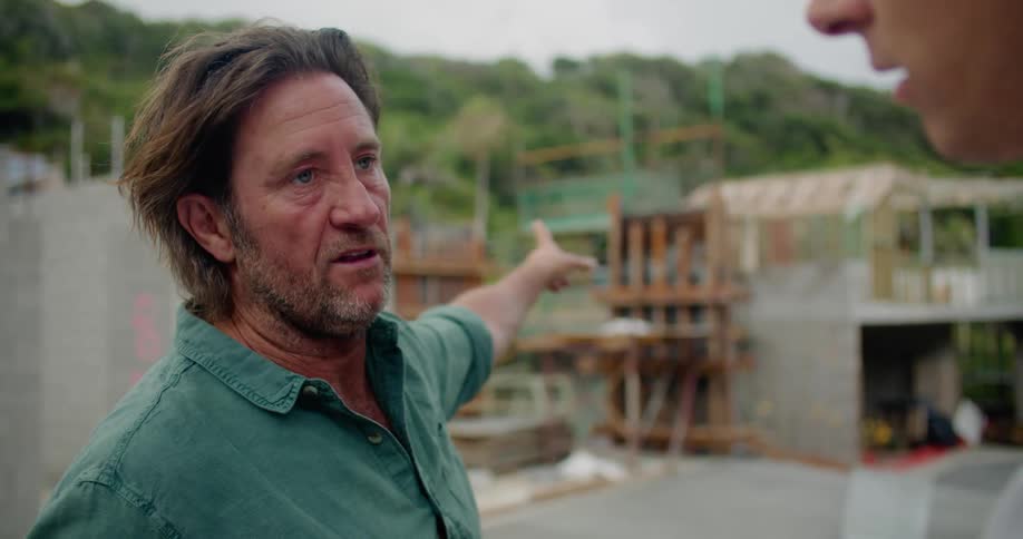 A man nods while pointing towards the construction site