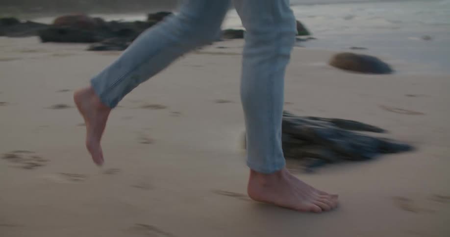 Man with jeans and blue shirt runs on the beach next to sea