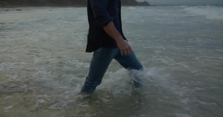 Blonde man with blue shirt and jeans walks into ocean