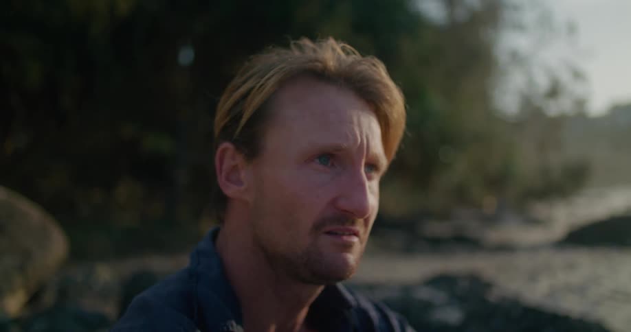 Man sits on beach frowning before he starts crying then wiping his face