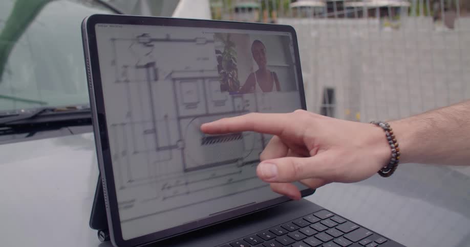 A man scrolls a blueprint on a laptop sitting on a car hood while having a video call