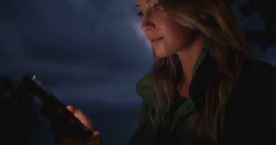 A women is outside holding and scrolling on a cell phone on a windy night