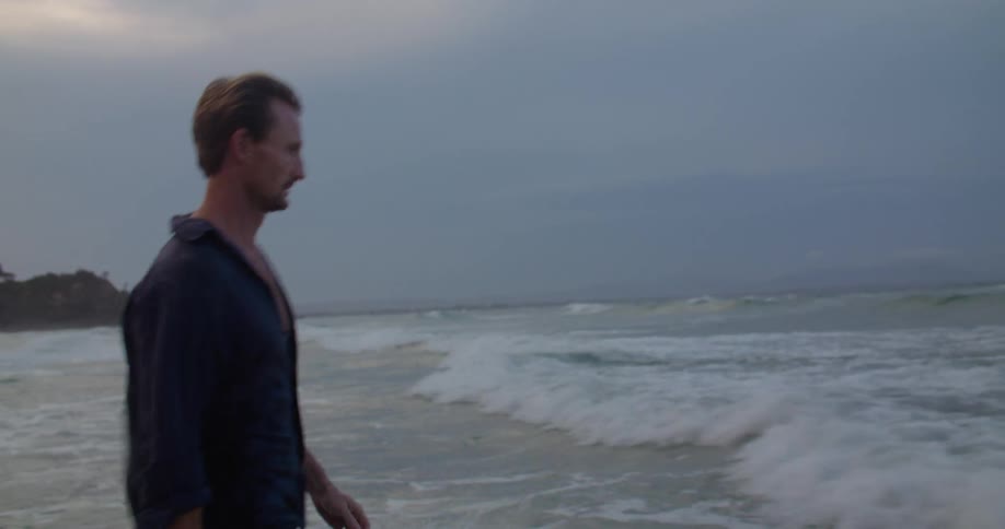 A man wades deeper into the ocean in jeans