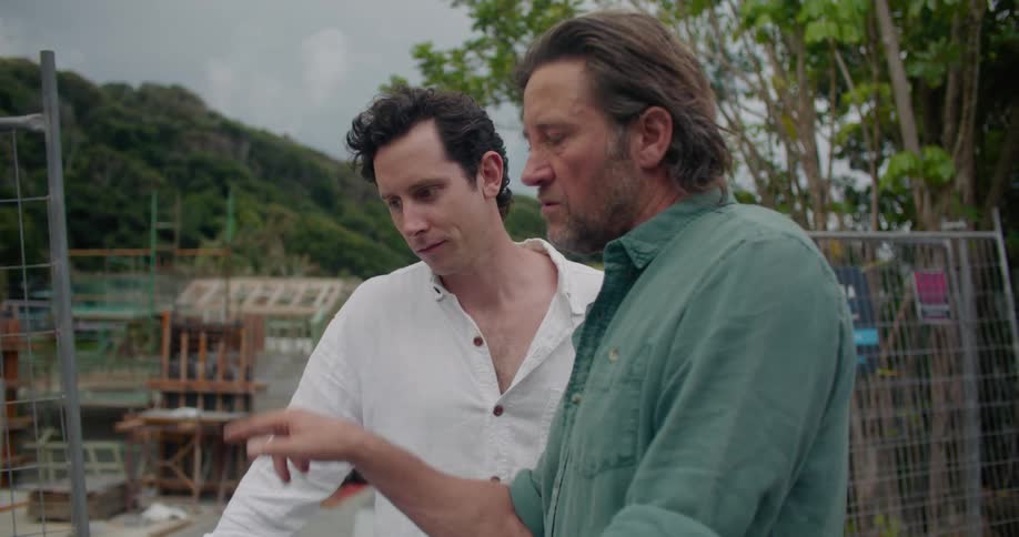 Two men are looking at a laptop and talking at a building construction site