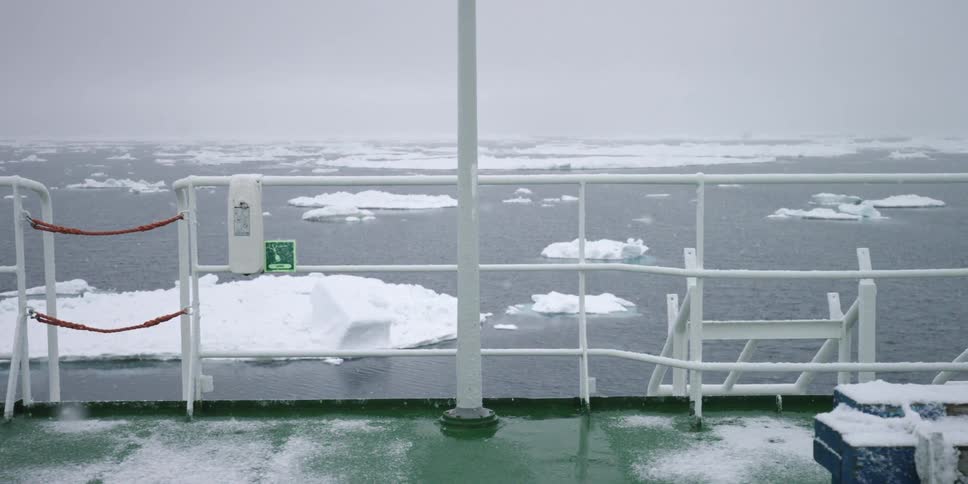 Ice floats in the water below a railing
