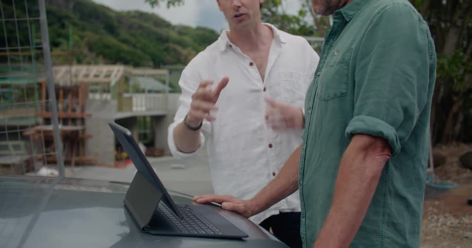 Coworkers stand near car at construction site consulting computer