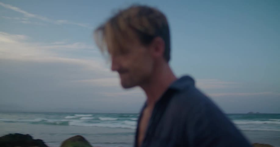 A man drinks from a bottle as he walks on the beach