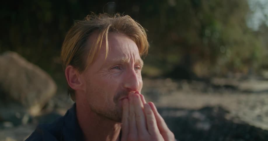 A man wipes tears from his eyes while sitting on the beach