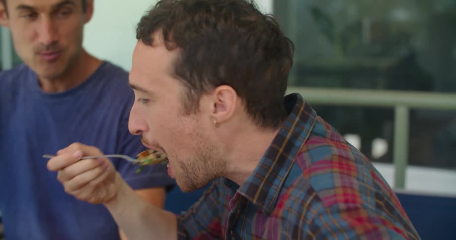 Young male couple talking while eating a meal on the porch at home
