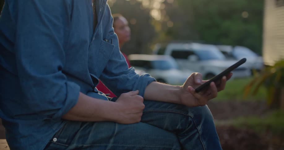 Young man sitting on the backyard at home checking his phone at sunset