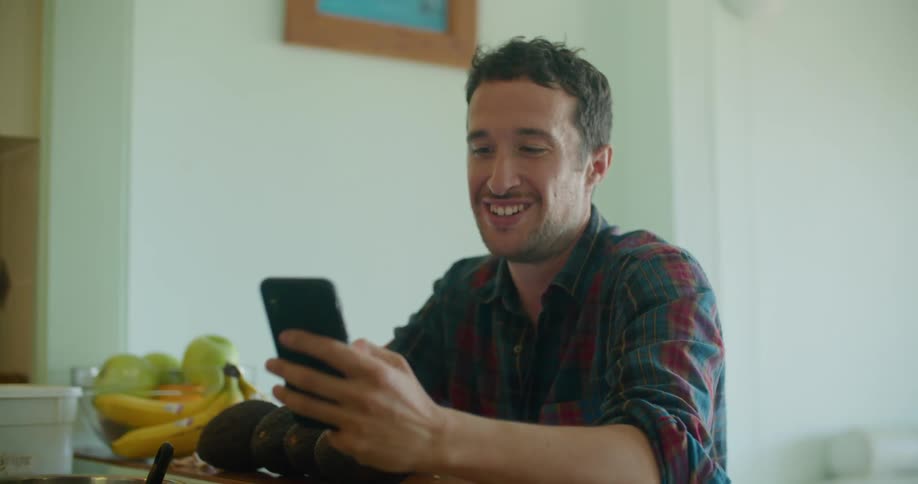 Young man sitting in the kitchen at home shows an image on his phone to a his partner