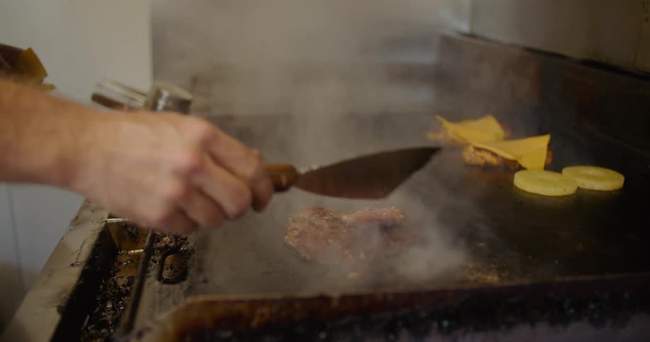 A man is cooking burgers on the stove