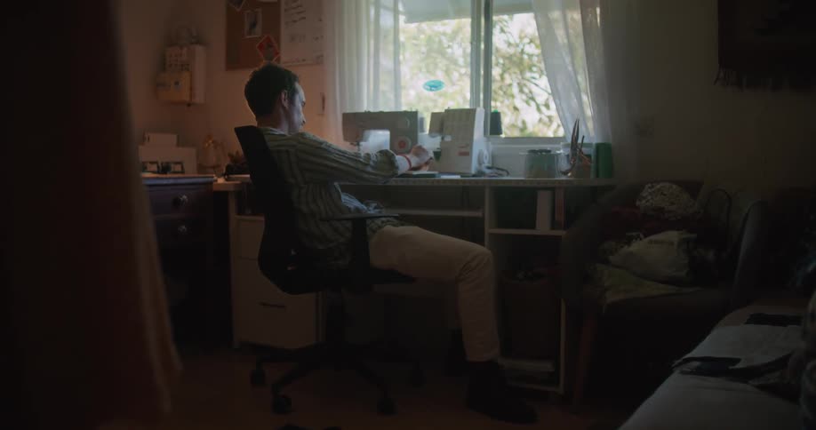 A man is sitting in a sewing room in a home while thinking during the day