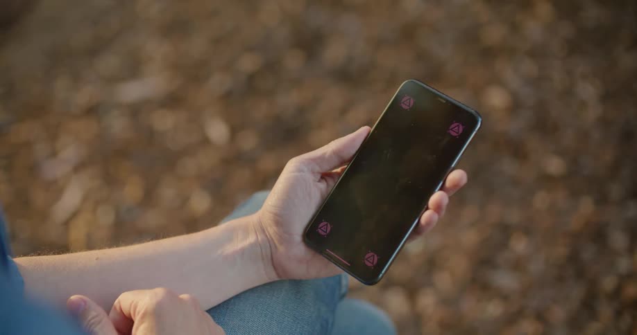 A man sits crosslegged outside and looks at his phone