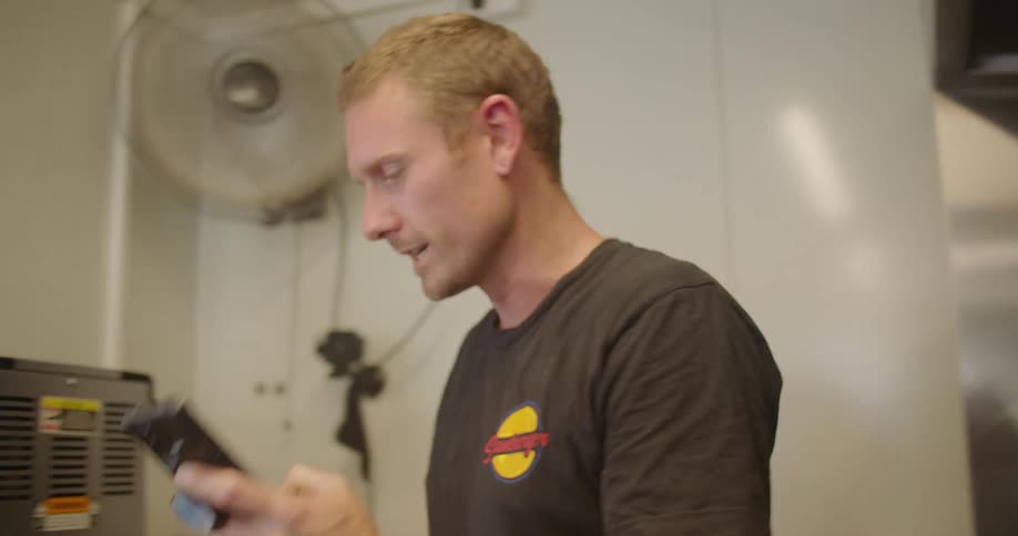 Man working at a restaurant kitchen ends a call on his smartphone to talk to customers