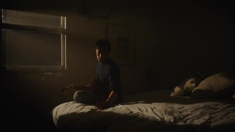 A man is playing guitar on his bed at night