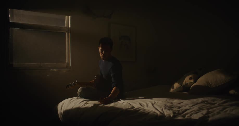 A man is playing guitar on his bed at night