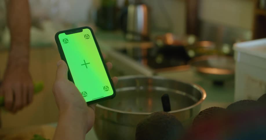 A person holds their phone while the other cooks
