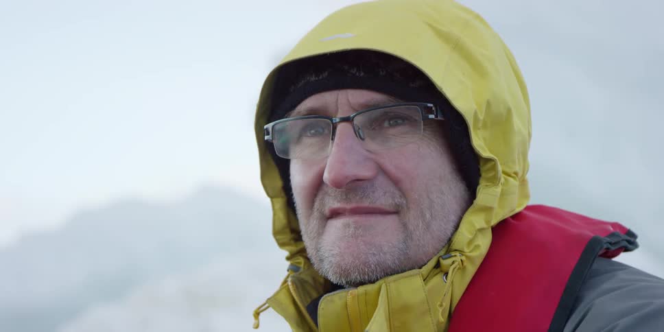 A man wearing glasses, a yellow jacket, and red life vest is looking into the distance while moving