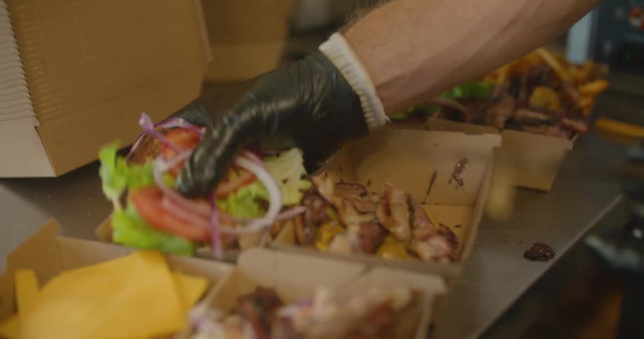 A person is putting burgers together in the cartons