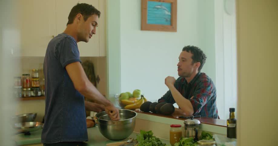 In a home one man is preparing a salad in a kitchen and lets another man have a taste