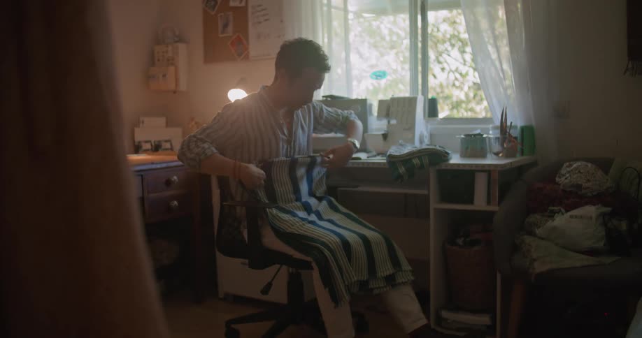 Man sitting on a sweing workshop folding cloth near a window